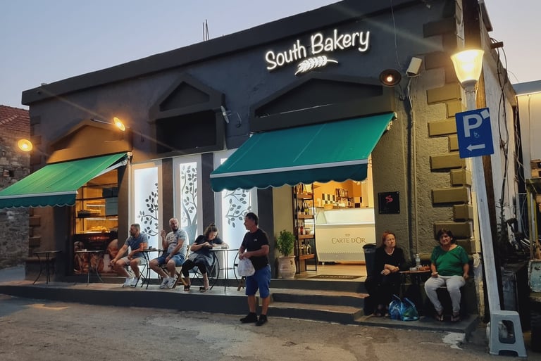 Customers sitting outside South Bakery at dusk with green awnings and glowing shop lights.