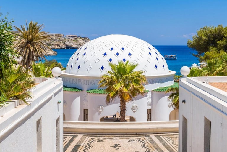 White domed building with blue tiles at Kallithea Springs in Rhodes, Greece overlooking the sea.