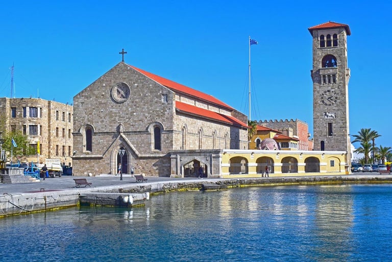 The historic Church of the Annunciation and stone clock tower on the Rhodes waterfront.
