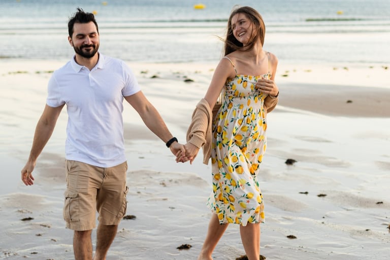 Couple holding hands, walking barefoot along a golden Algarve beach, smiling