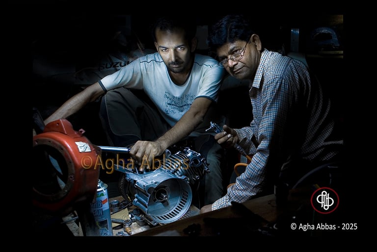 Two mechanics, one in Suzuki T-shirt, repairing an engine with a wrench in a workshop.