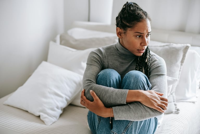 Concerned young woman sitting on a bed hugging her knees, reflecting mental health and anxiety.