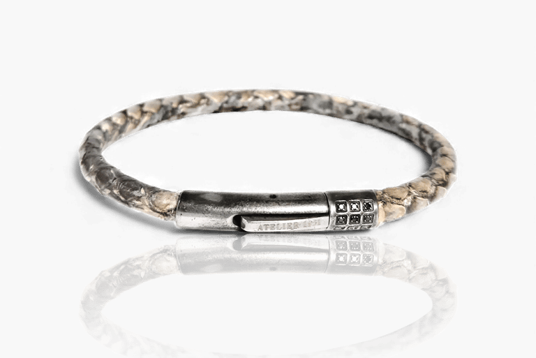Handcrafted python leather cord bracelet with a brushed silver magnetic clasp on a reflective white surface.