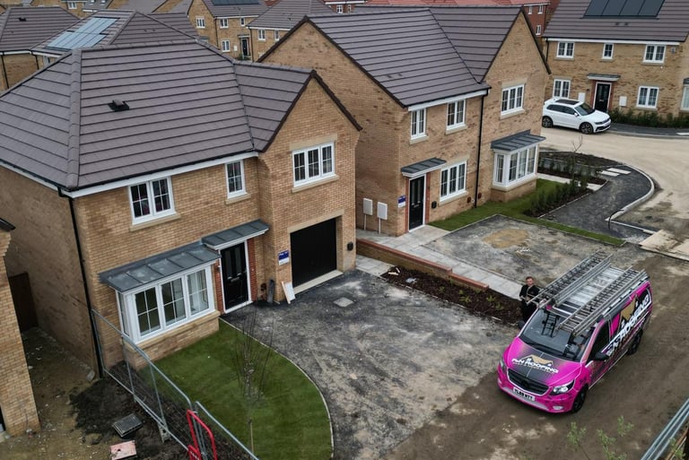 New build brick houses on a modern housing estate with a pink roofing contractor van parked in the driveway.