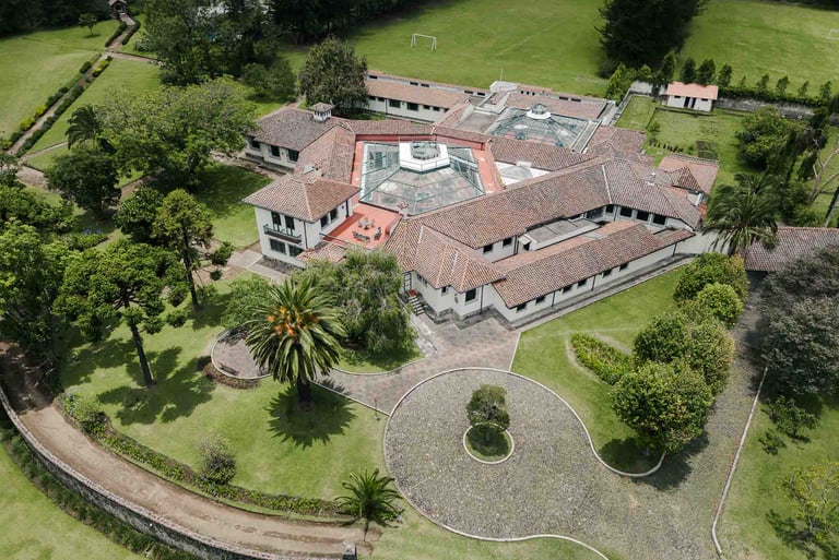Fotografía con dron de mansión colonial de paredes blancas con techo naranja, cúpulas rodeada de naturaleza Quito Ecuador