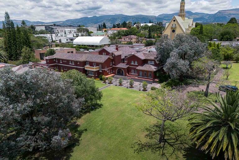 Fotografía aérea de gran casa religiosa de color rojo rodeada de hermoso  jardín verde en Quito Ecuador