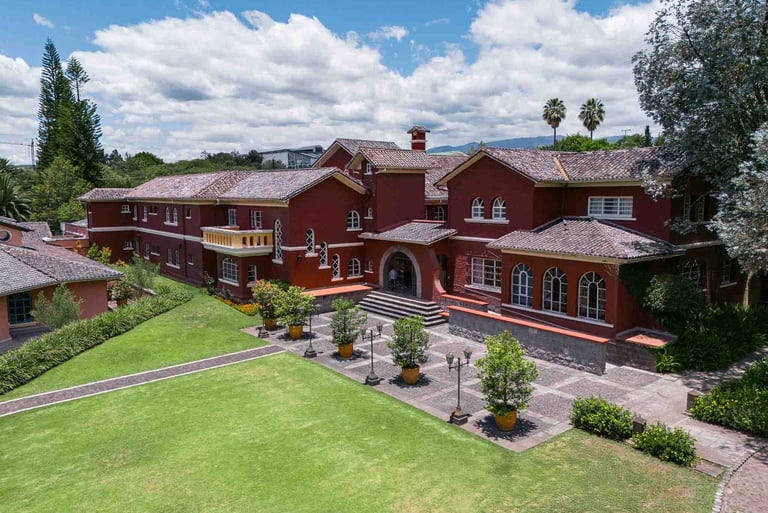 Fotografía aérea de gran casa religiosa de color rojo rodeada de hermoso  jardín verde en Quito Ecuador