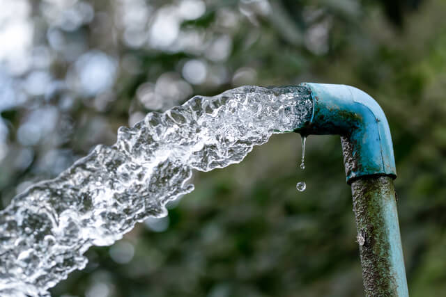 Fresh clean water flowing from a blue metal pipe for irrigation and agriculture.