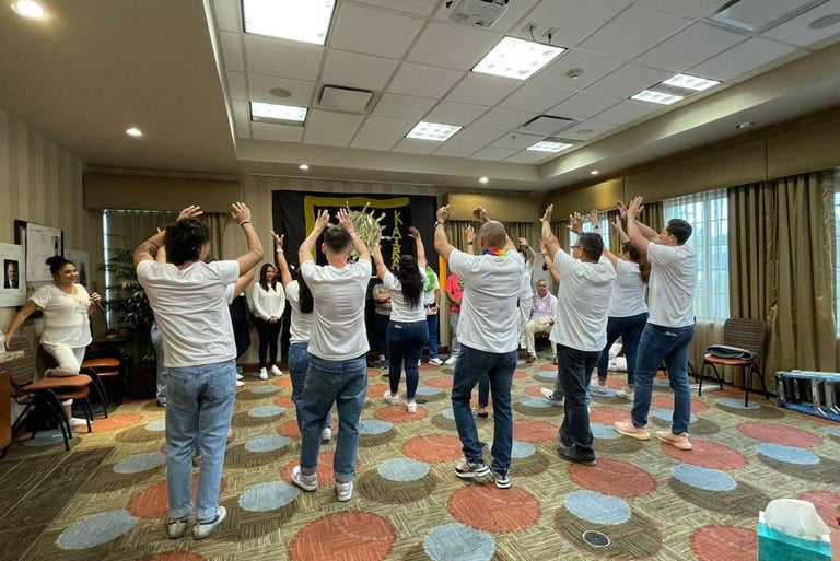 A group of people wearing white shirts and jeans participating in a team-building workshop activity in a conference room.