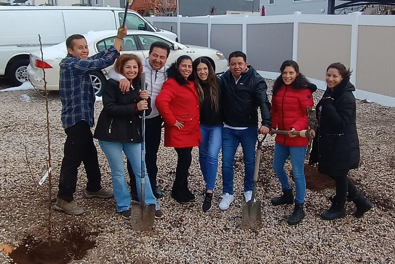 A group of smiling family members planting a new tree in their backyard with shovels.