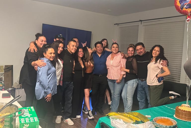 A large happy family celebrates a birthday party together in a living room with food and balloons.