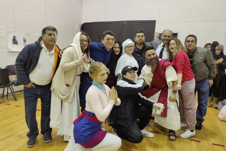 A diverse group of friends posing in a community hall wearing various costumes for a theatrical play or celebration.