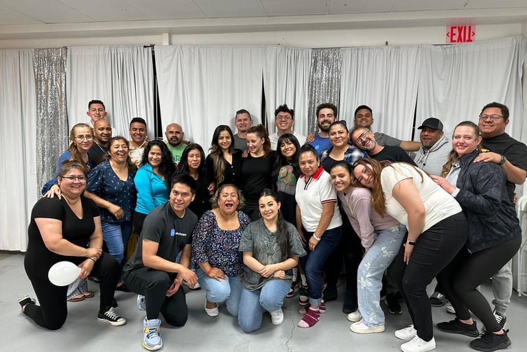 A large, diverse group of smiling people posing for a community group photo in front of white curtains.
