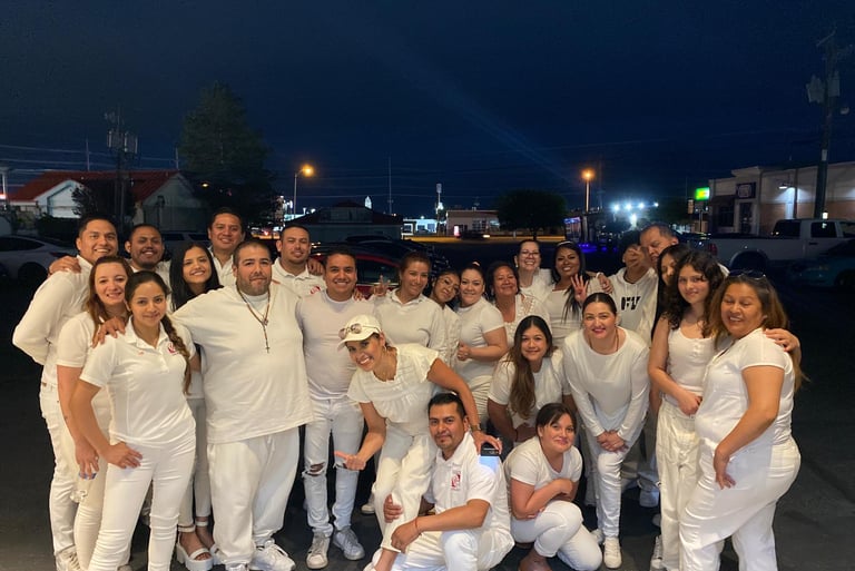 A diverse group of friends smiling and posing for a group photo outdoors at night wearing all white clothing.