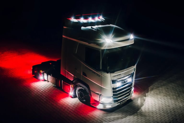 White DAF semi-truck with illuminated headlights and red underglow lighting parked on a stone lot at night.