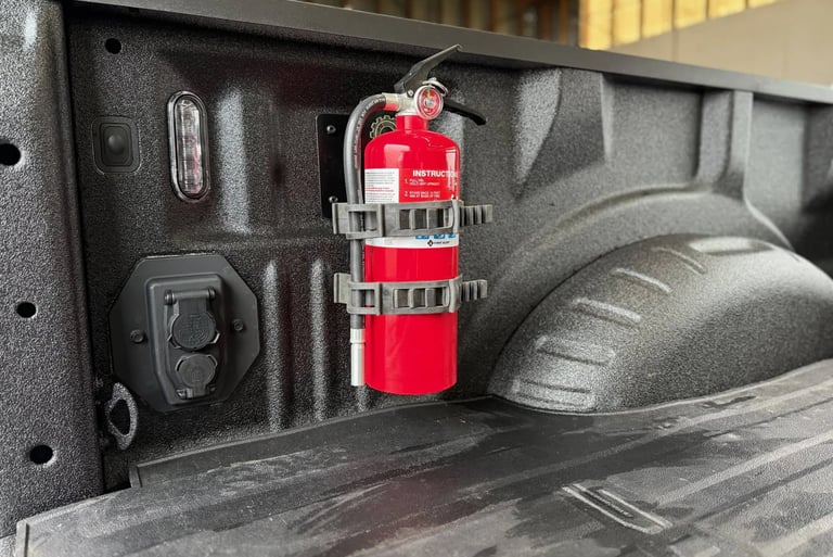 A red fire extinguisher mounted to the side wall of a pickup truck bed using a heavy-duty bracket.