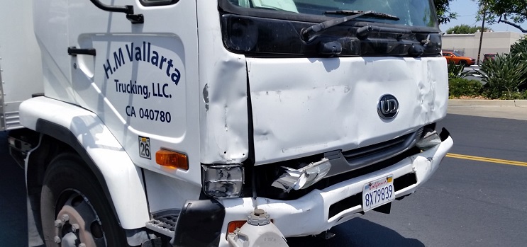White commercial delivery truck with front end damage to the bumper and hood after a vehicle accident.