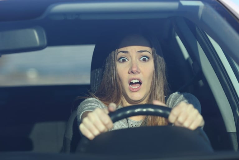 Scared woman driver looking shocked and terrified behind the steering wheel while driving a car.