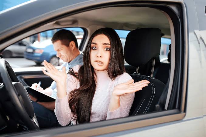 Anxious young woman taking a driving test with a nervous expression while the instructor takes notes.