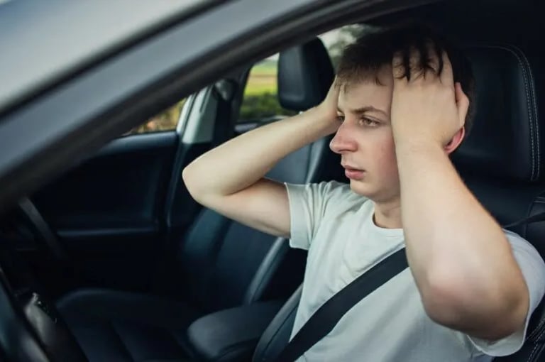 A stressed driver holding his head in frustration while sitting in a car seat after a breakdown.