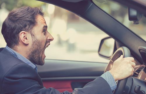 Angry businessman screaming behind the steering wheel while experiencing road rage during commute.