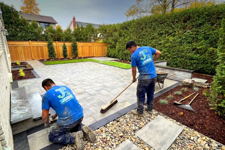 Professional landscapers installing a custom stone paver patio and backyard garden beds In New York
