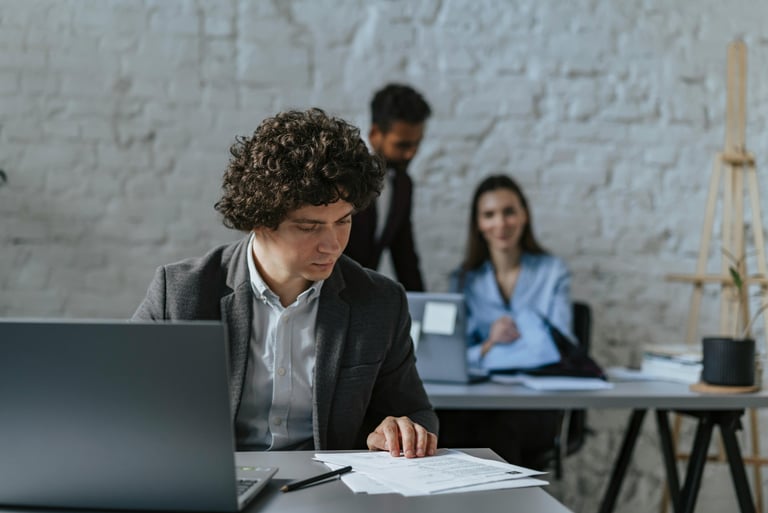 Professional businessman reviewing documents at a laptop in a modern industrial office space.