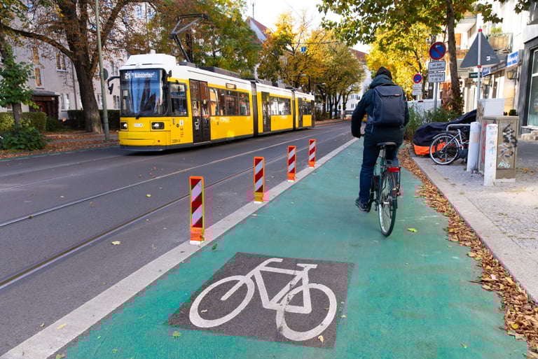 Bild von einer Straße mit grünem Fahrradweg. Auf der anderen Straßenseite fährt eine Straßenbahn.