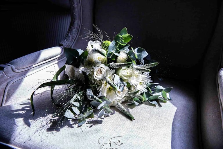 Elegant white wedding bouquet with roses and eucalyptus leaves resting on a vintage armchair.