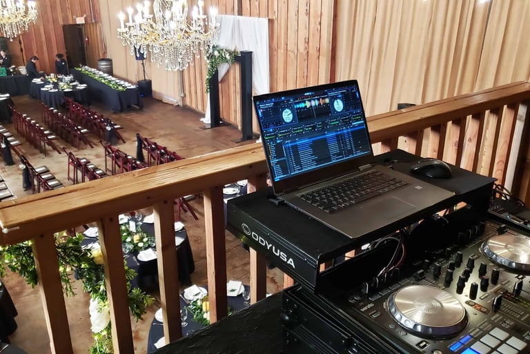 A DJ booth setup on the balcony of an event venue overlooking a wedding ceremony space.