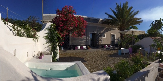 Luxury villa courtyard with a plunge pool, blooming bougainvillea, and palm trees under a blue sky.