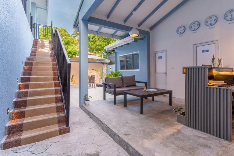 Modern hotel reception area with outdoor lounge seating, front desk, and stone stairs.