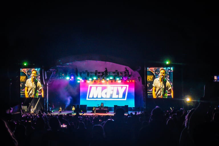 British pop rock band McFly performing live on a brightly lit concert stage for a large crowd at night.