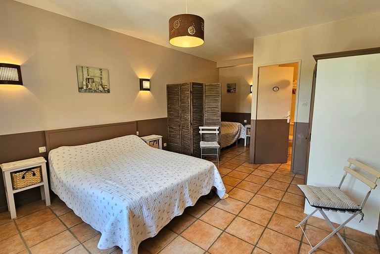 Chambre chocolat avec un grand li et un petit lit séparé d'un paravent avec salle de bain.