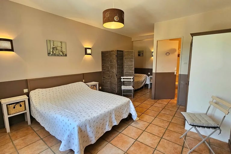 Chambre chocolat avec un grand li et un petit lit séparé d'un paravent avec salle de bain.