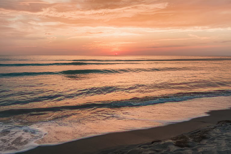 A tranquil beach scene at sunset, with calm waves lapping at the shore and a warm, golden sky