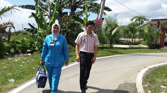 A healthcare nurse and doctor walk along a village road for a community home visit.