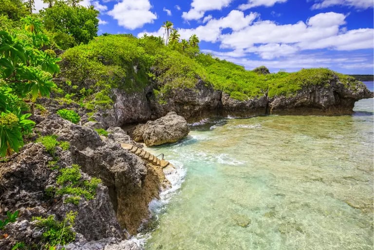 Tropical rocky coastline with stone steps leading into clear turquoise ocean water under a blue sky.