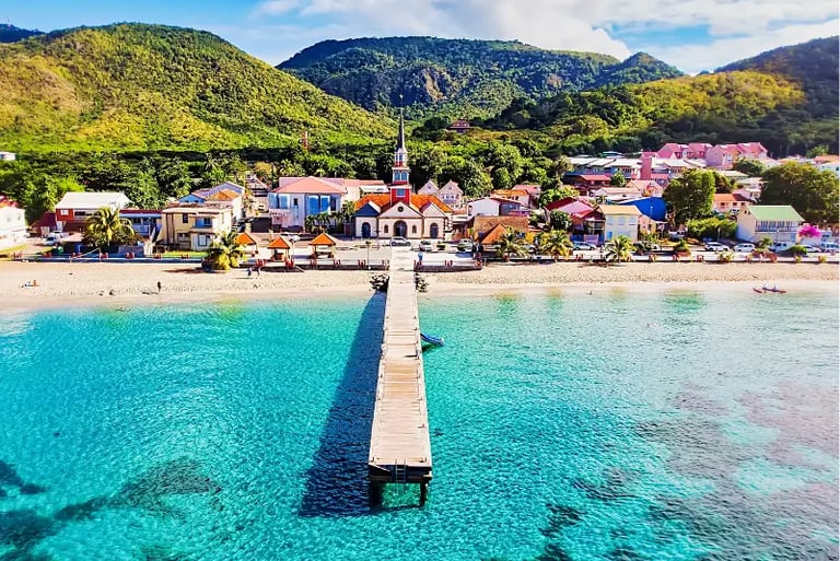 Aerial view of Anse d'Arlet beach in Martinique featuring a wooden pier, turquoise water, and a historic church.