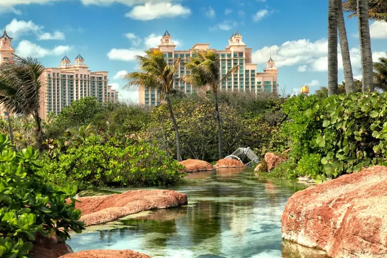 Luxury Bahamas resort towers overlooking a tropical lagoon with palm trees and rock formations.