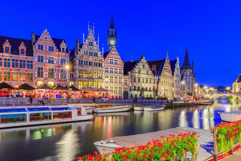 Illuminated medieval guildhouses and canal boats at Graslei and Korenlei in Ghent, Belgium at twilight.