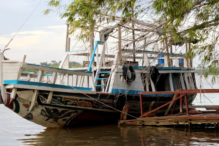 Hand-painted traditional wooden boat docked on a tropical river under leafy bamboo trees.