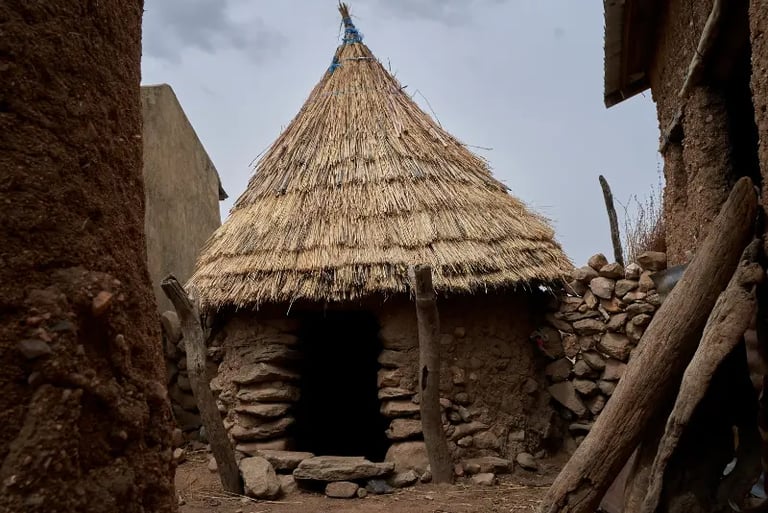Traditional African mud hut with a conical thatched straw roof and stone entrance in a rural village.