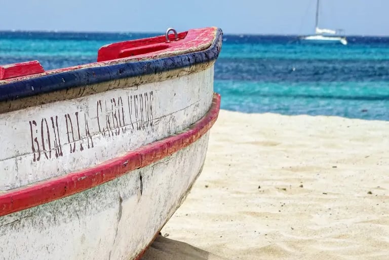 Rustic wooden fishing boat on a sandy beach in Cape Verde with turquoise ocean water in the background.