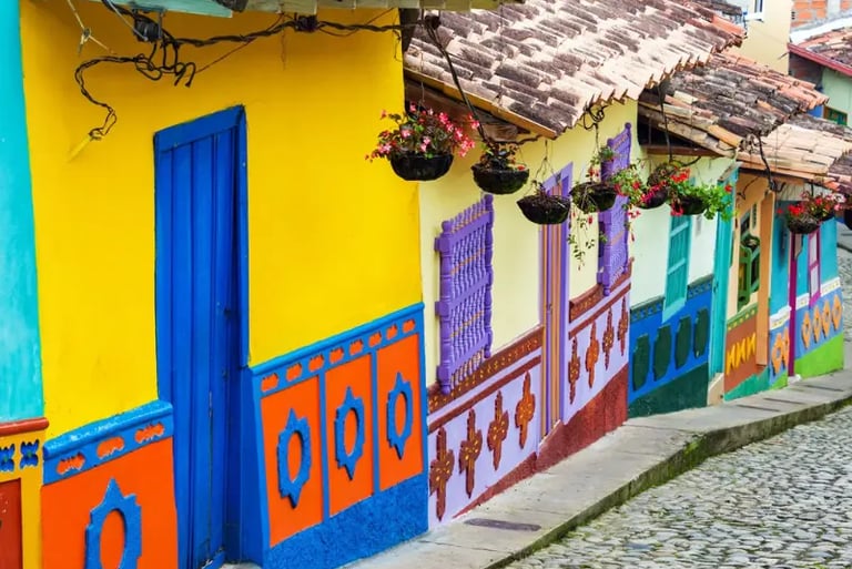 Brightly colored colonial houses with flower baskets on a cobblestone street in Guatape, Colombia.