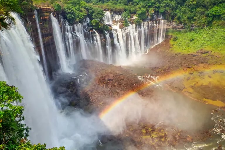 Scenic view of Kalandula Falls in Angola with a vibrant rainbow arching over the mist and rocky basin.