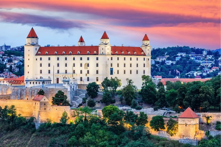 Bratislava Castle at sunset with a vibrant orange and purple sky over the white hilltop fortress in Slovakia.