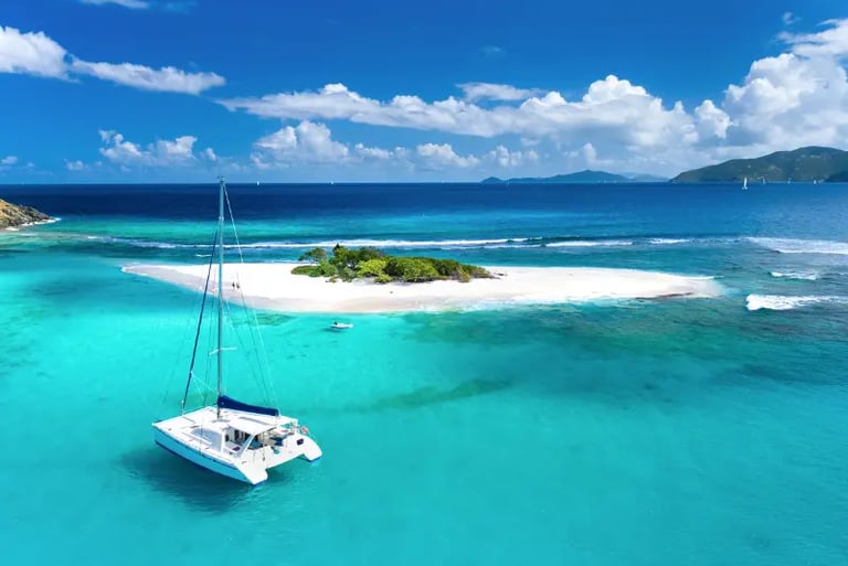 White sailing catamaran anchored in turquoise tropical waters near a sandy island cay under a blue sky.