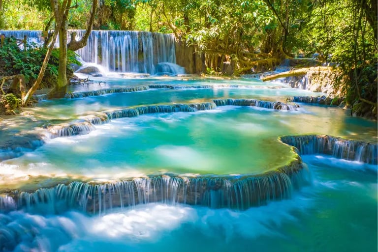 Kuang Si Falls features turquoise tiered pools and cascading waterfalls in a lush tropical jungle.
