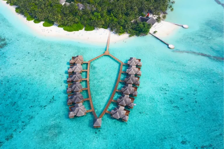 Aerial view of luxury overwater bungalows and turquoise ocean at a tropical Maldives island resort.